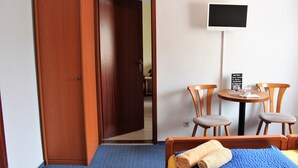 A hotel room with a wooden wardrobe, a bed with a blue bedspread, a TV on the wall, and two wooden chairs around a small table. - Pension An der Kamske (Lübbenau/Spreewald)