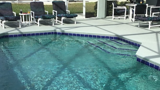 Ein klares Schwimmbecken mit blauen Fliesen, umgeben von weißen Liegestühlen und einem überdachten Bereich.