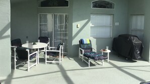 Ein überdachter Patio-Bereich mit Tisch und Stühlen, einem überdachten Grill und einer Schiebetür.