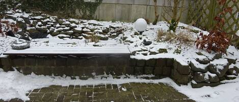 A snow-covered stone bench with a snowball and a spherical object nearby.