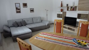 En moderne stue med en grå sofa, et træspisebord med et stribet dug og et fladskærms-tv.