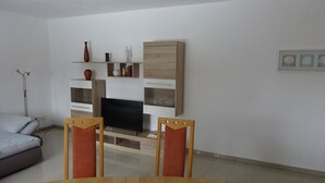 En stue med fjernsyn, sofa, sofabord og spisebord med stole.