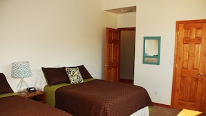 Une chambre avec deux lits, une table de chevet avec une lampe, une porte en bois et un miroir au mur.