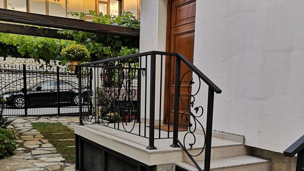 A stone-paved pathway leading to a building with a wooden door and a black metal railing. - Cozy house near the gondola in Bansko.  (Bansko)