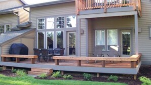 A two-story house with a deck, outdoor seating, and a covered grill area.