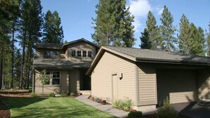 A two-story house with a garage, surrounded by a well-maintained lawn and tall pine trees.