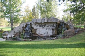 Ein Steinschild mit der Aufschrift 'Widgi Creek', umgeben von einem kleinen Wasserfall und Felsen.
