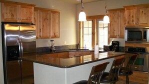 A modern kitchen with wooden cabinets, stainless steel appliances, a large island with bar stools, and pendant lighting.