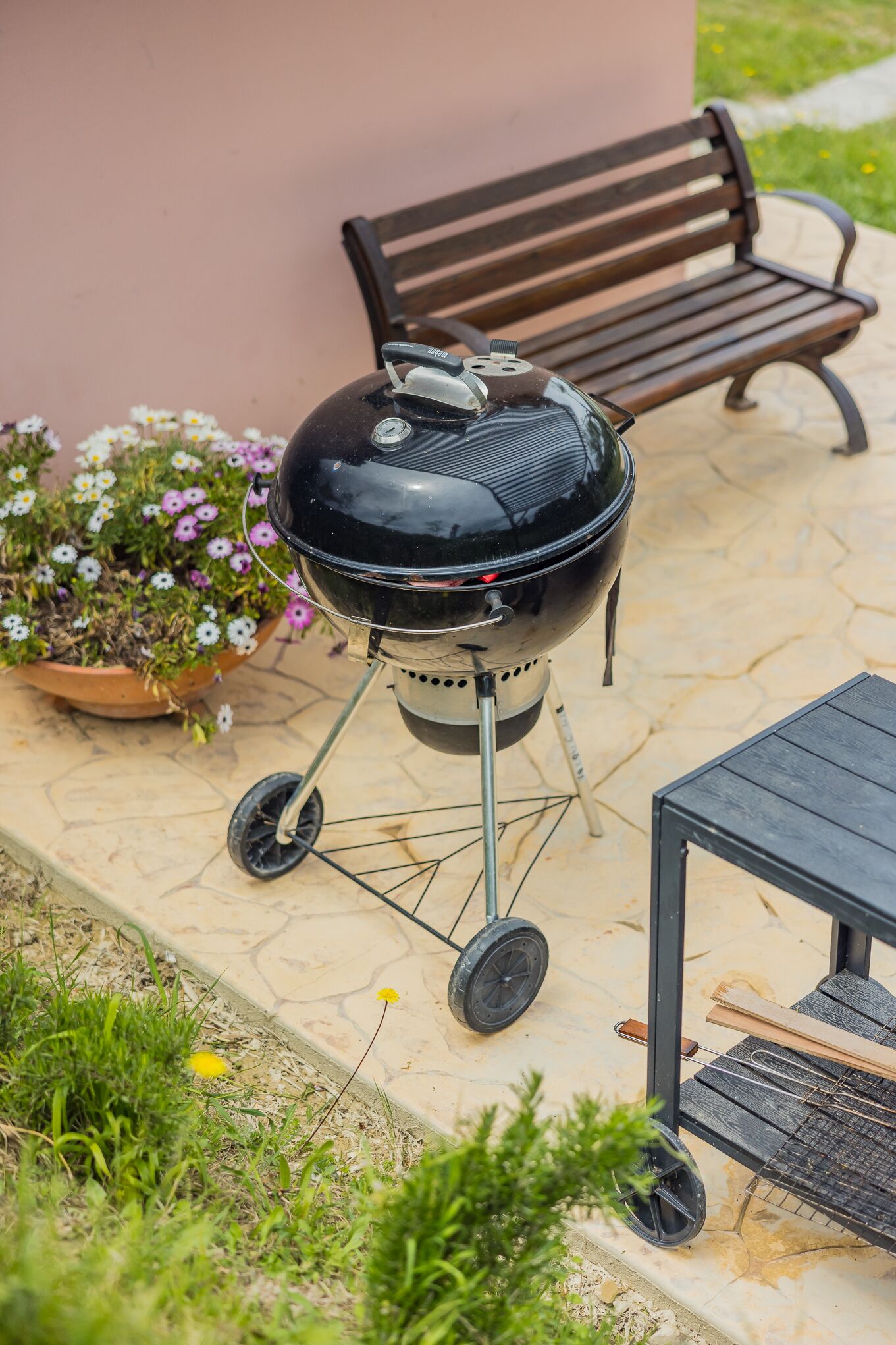 A portable barbecue grill on a patio with a bench and a table nearby.