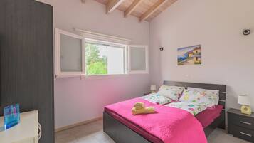 A bedroom with a bed, a window, a nightstand, and a painting on the wall.