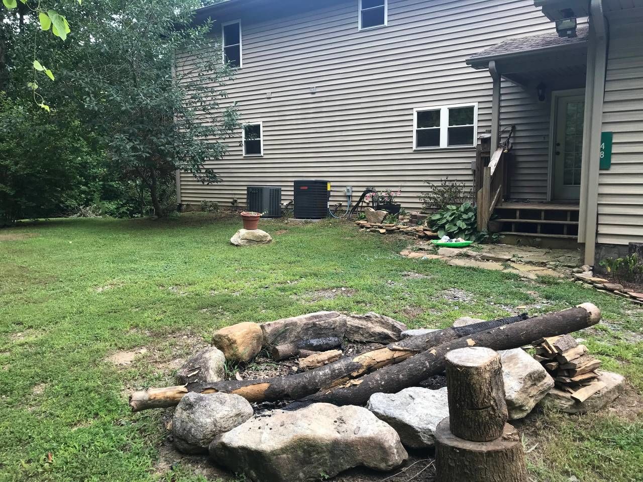 A house with a front yard containing a fire pit and logs.