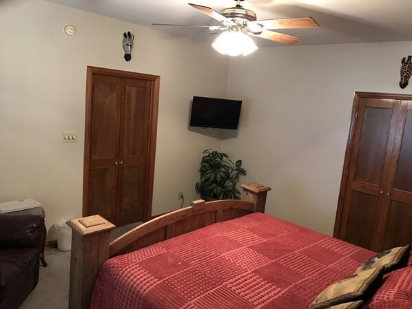 Un dormitorio con una cama de madera, un ventilador de techo, un televisor en la pared y una planta.