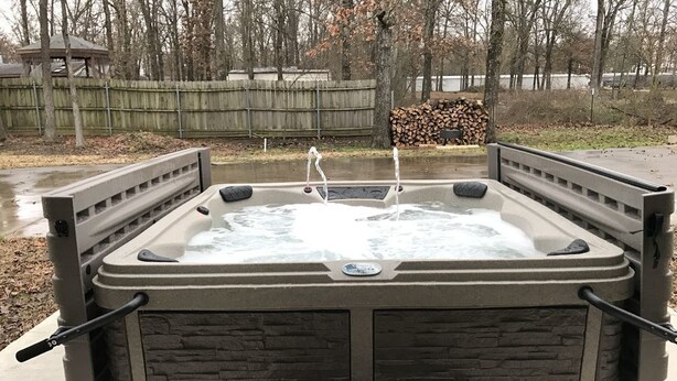 A hot tub with a stone facade, a wooden deck, and a view of a wooden fence and trees. - Family Friendly Lake House Located at Mid-west arm of Lake Fork (Quitman)
