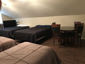 Una habitación con dos camas, una mesa de comedor con sillas y un televisor de pantalla plana sobre un soporte.