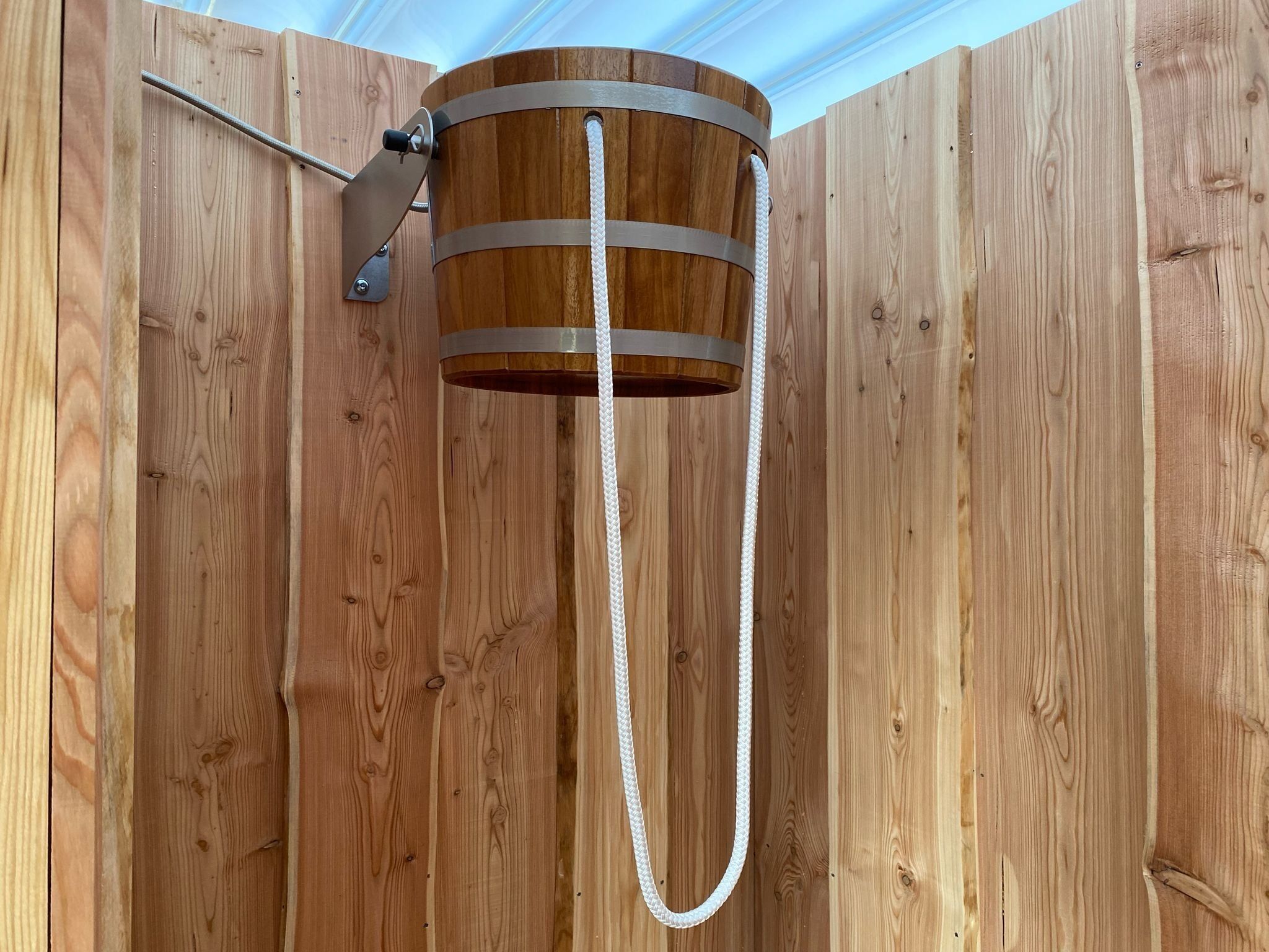 A wooden barrel-shaped object with a metal band and a rope attached, mounted on a wooden wall.