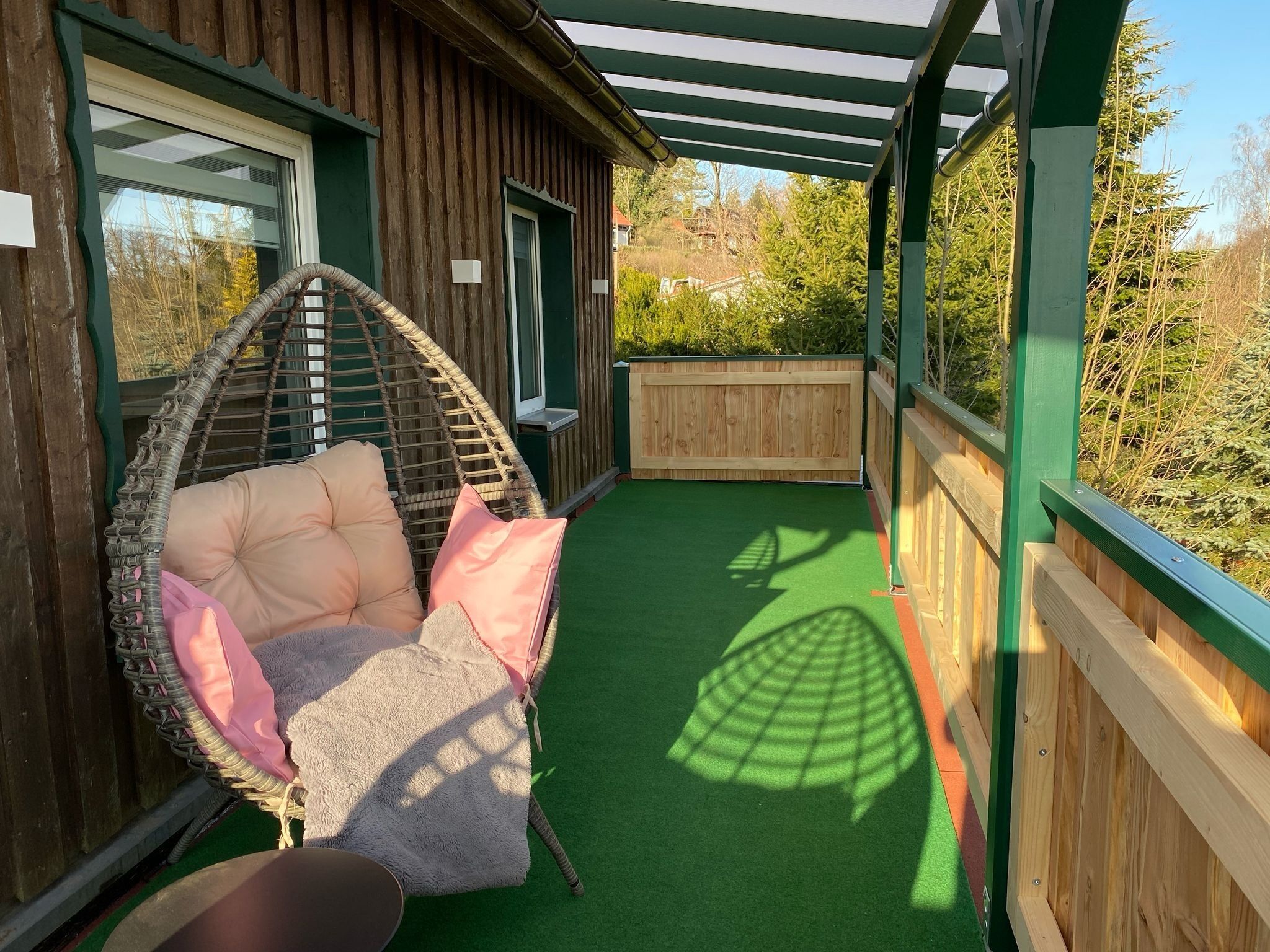 A wooden cabin with a green roof, a hanging chair with cushions, and a green artificial turf floor.