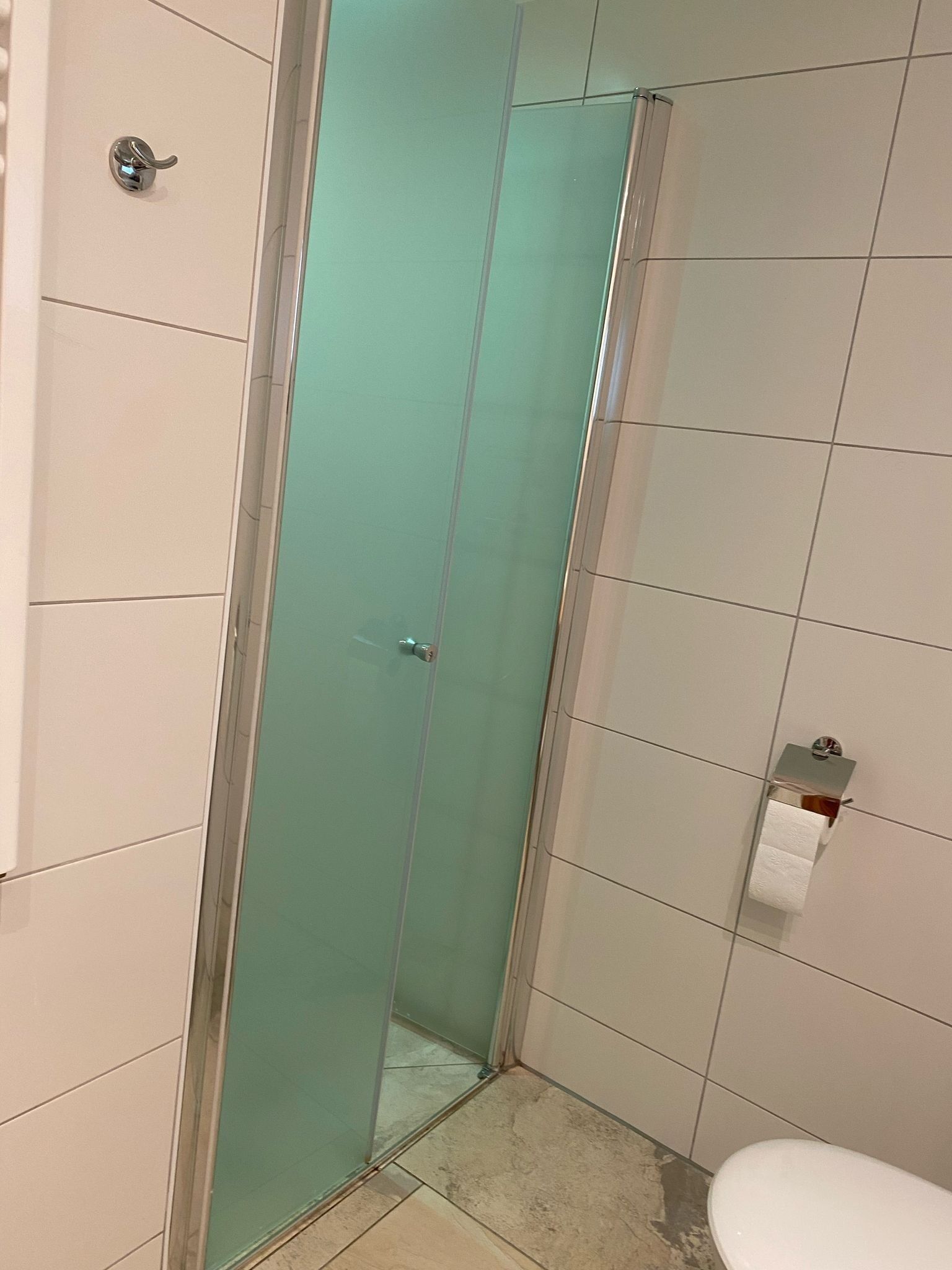 Een badkamer met een douchecabine van glas, een toilet en een papieren handdoekdispenser.