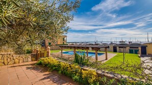 Ein Poolbereich mit Pergola, Steinmauer und Blick auf das Meer mit Booten.