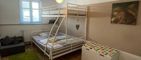 Una habitación pequeña con literas, un sofá compacto, un radiador, una ventana con persianas y un cuadro en la pared.