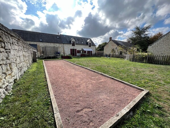 A courtyard with a gravel court, stone walls, and a house with a sloped roof.