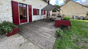 Een stenen huis met rode luiken, een houten terras en een overdekte patio.