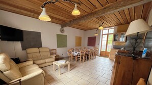 Een ruime woonkamer met een bank, stoelen, een eettafel en een keukenhoek.