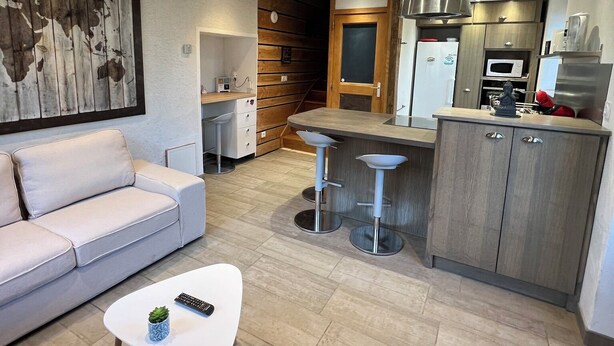 Een moderne keuken met een centraal eiland, een eethoek met een witte tafel en stoelen, en een woonkamer met een bank en salontafel.
