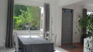 En matplats med ett bord dukat för två personer, en vas med blommor och utsikt över grönskan utanför.