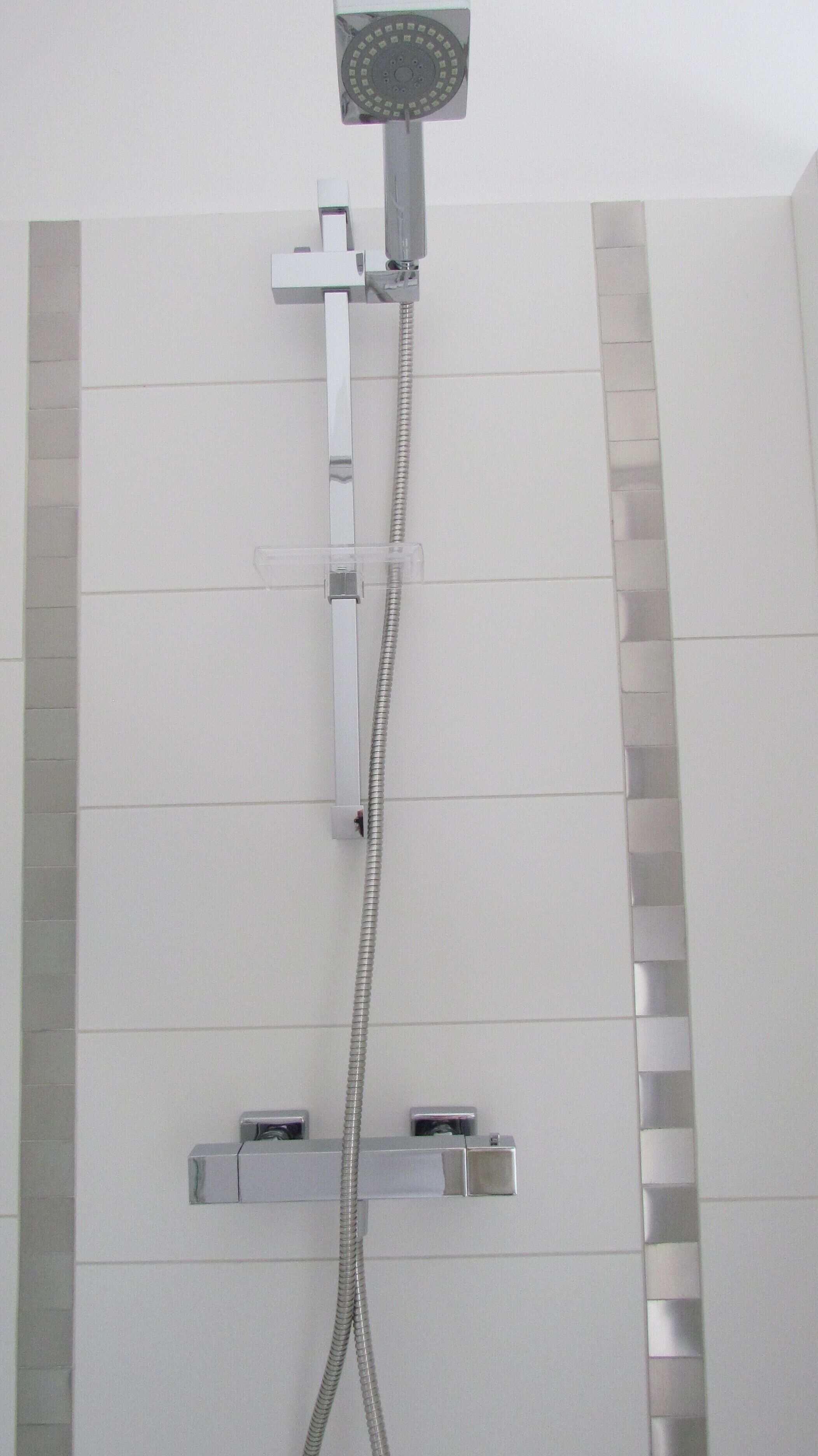 Une douche équipée d’un pommeau de douche à main, d’un pommeau de douche fixe et d’un accessoire de douche à main.
