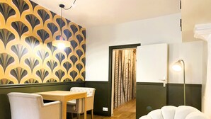 Una habitación con papel tapiz estampado, una mesa de comedor de madera con sillas, un sillón blanco y una lámpara.