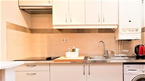 Una cocina moderna con armarios blancos, encimera de acero inoxidable, lavavajillas integrado y hervidor rojo.