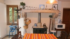 Een eethoek met een geruite tafelkleed, houten stoelen, een fornuis en diverse keukenspullen aan de muur.