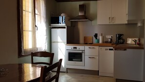 A compact kitchen with white appliances, including a microwave, oven, and dishwasher. There is a wooden table and chairs, and a window allowing natural light. - Gites de Mon Clocher 2 apartments in a village house (Alpes-Maritimes)