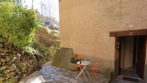 A stone pathway leading to a small outdoor seating area with a table and chairs, a stone wall, and a door. - Gites de Mon Clocher 2 apartments in a village house (Alpes-Maritimes)
