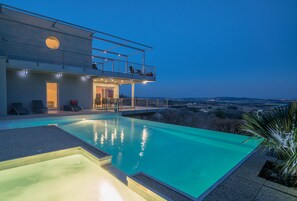 Une maison moderne dotée d’une piscine, d’un balcon avec des chaises et offrant une vue sur le paysage.