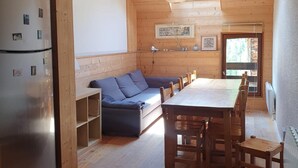 Eine kleine Küche mit Holzausbau, einem Einbaukühlschrank, einem Esstisch mit Stühlen und einem blauen Sofa.