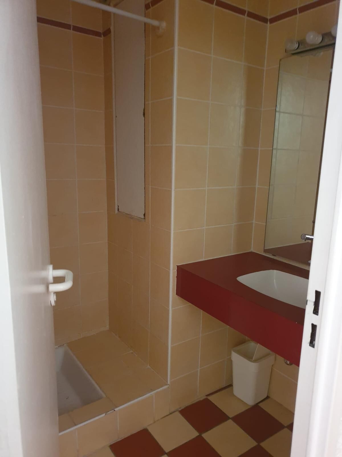 Een badkamer met een rode wastafel, een spiegel, een douchegedeelte en een witte prullenbak.