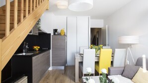 A modern kitchen with wooden staircase, a dining area with a yellow chair, and a living room with a sofa and a lamp. - Beautiful, warmly decorated apartment-1st line sea-Pool (Biscarrosse)