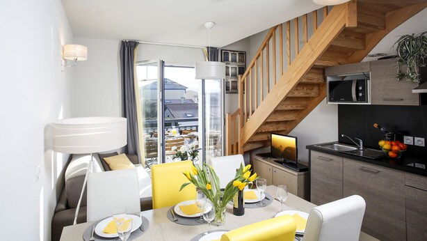 A modern kitchen with a wooden staircase, a dining area with yellow chairs, and a view of the outside. - Beautiful, warmly decorated apartment-1st line sea-Pool (Biscarrosse)