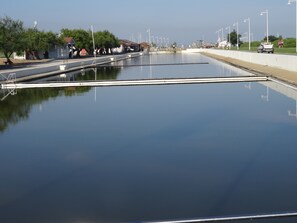Een rustig waterlichaam met een heldere lucht, een verharde wandelpad en wat groen.
