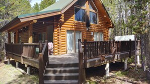 A log cabin with a porch, a staircase leading to the entrance, and a deck.