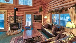 A log cabin interior with a stone fireplace, leather sofa, and a television.