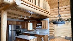 A log cabin-style kitchen with wooden cabinets, a stainless steel refrigerator, a microwave, and a hanging light fixture.