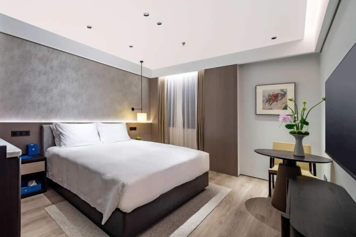 A modern hotel room with a large bed, bedside tables, a desk, and a chair.
