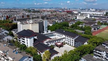 Un edificio alto con varios pisos, rodeado de vegetación y otros edificios.