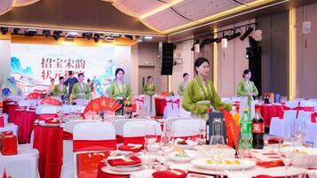 A banquet hall with round tables set for a formal event, featuring red and white tablecloths and a stage with a backdrop.