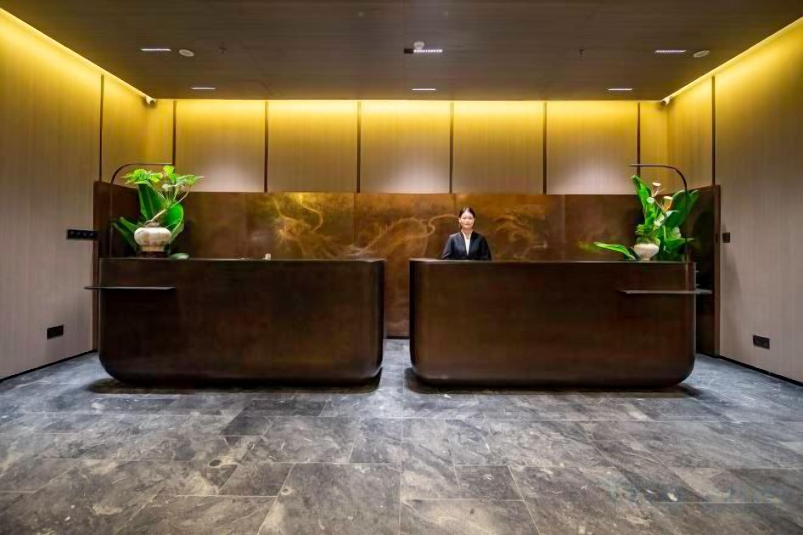 A reception area with two reception desks, a receptionist, and potted plants.