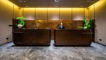 A reception area with two reception desks, a receptionist, and potted plants.