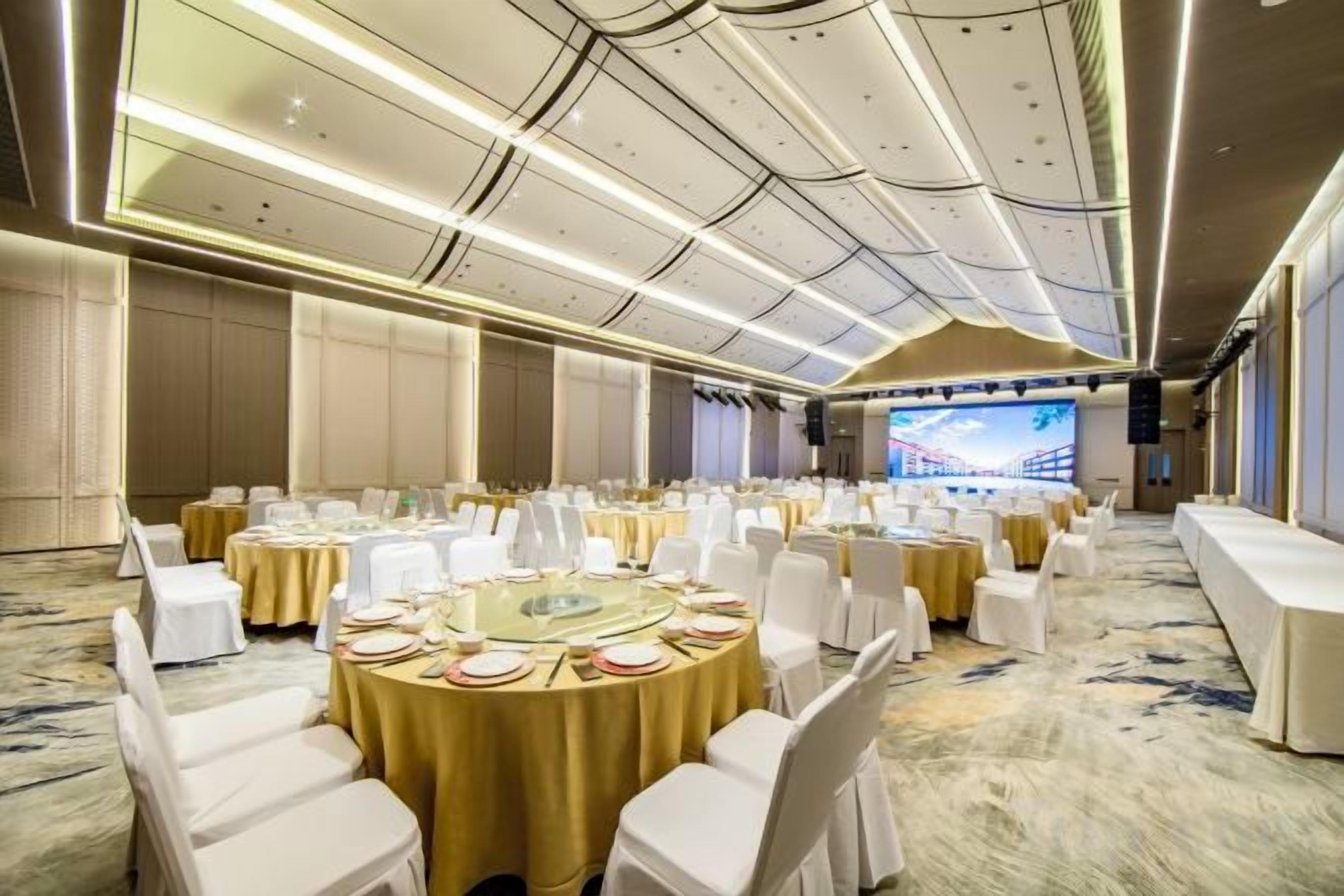 A banquet hall with round tables, white chairs, and a large screen displaying a bridge.