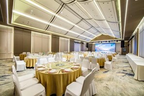 A banquet hall with round tables, white chairs, and a large screen displaying a bridge. - Ningbo Nanyuan Zhaobaoshan Hotel (Ningbo)
